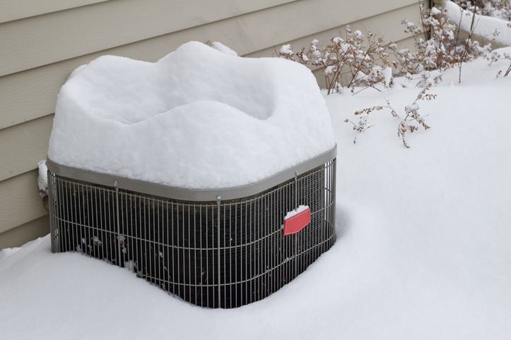 Close-up abstract view of an exterior HVAC system unit, covered with fresh deep snow following a winter blizzard.